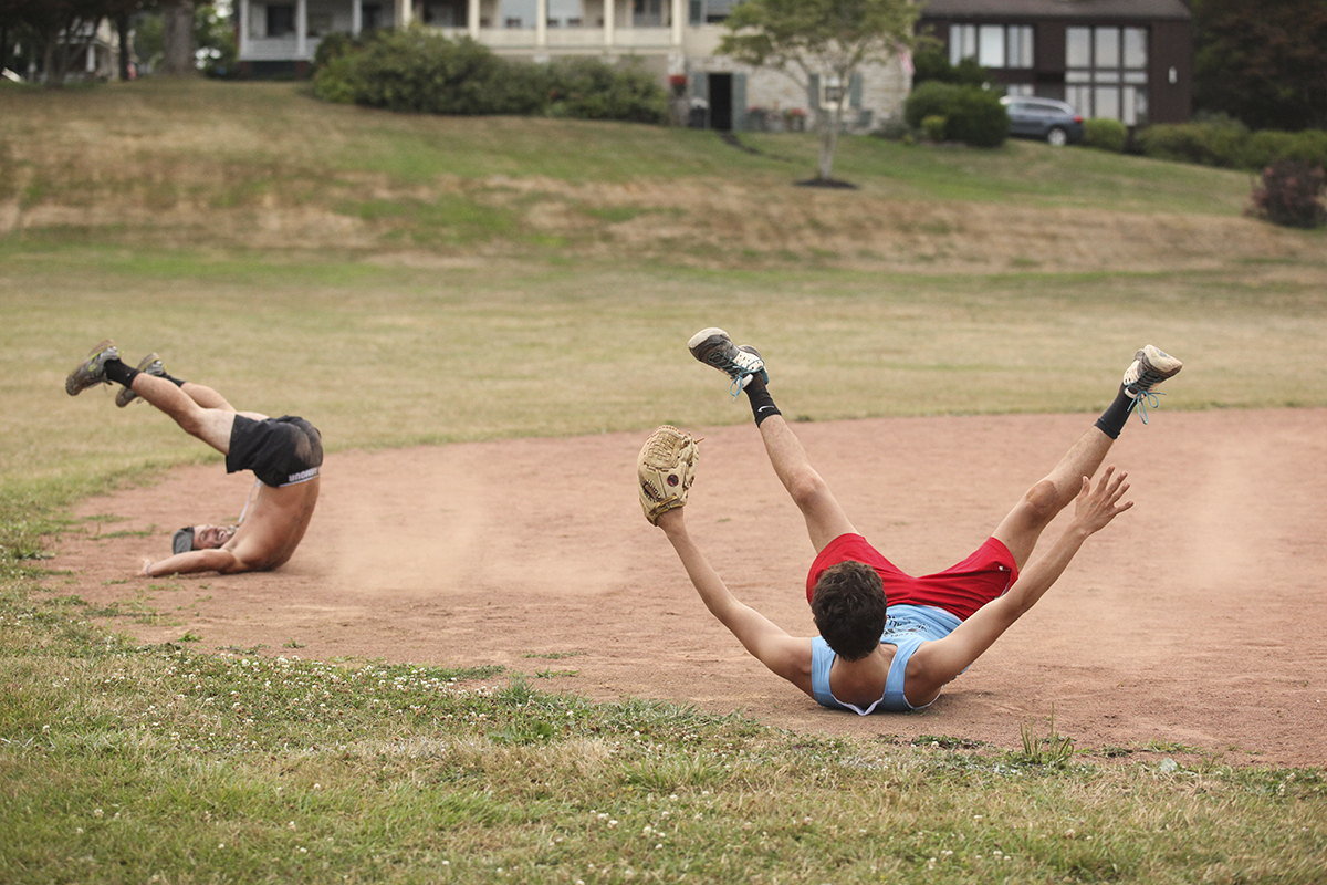 Skyler Zarou, left, and Peter Evans, right, members of the YAC PAC softball team, fall backwards after colliding in a celebratory mid-air body bump in honor of their softball team's victory over the Slugs team at 7 PM on Friday, July 29, at Sharpe Field. The YAC team beat the Slugs 21-5. Photo by Carolyn Brown.