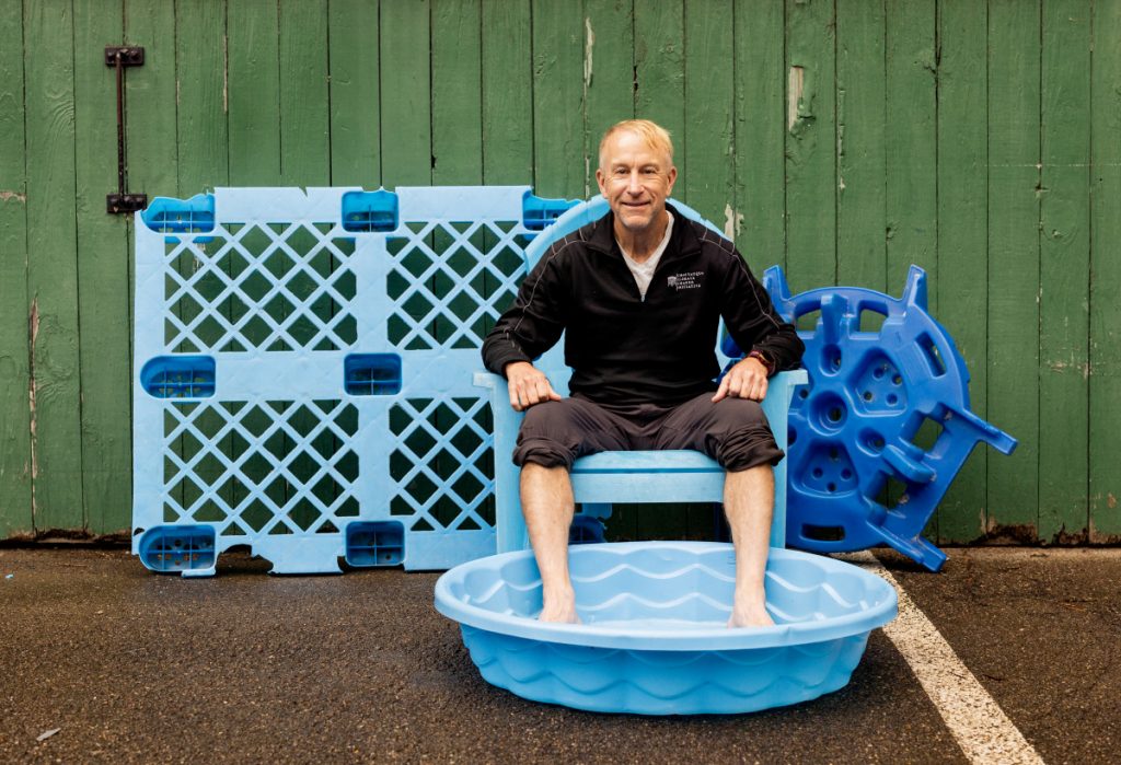 A man sits amid blue plastic to be recycled, with his feet in a kiddie pool.
