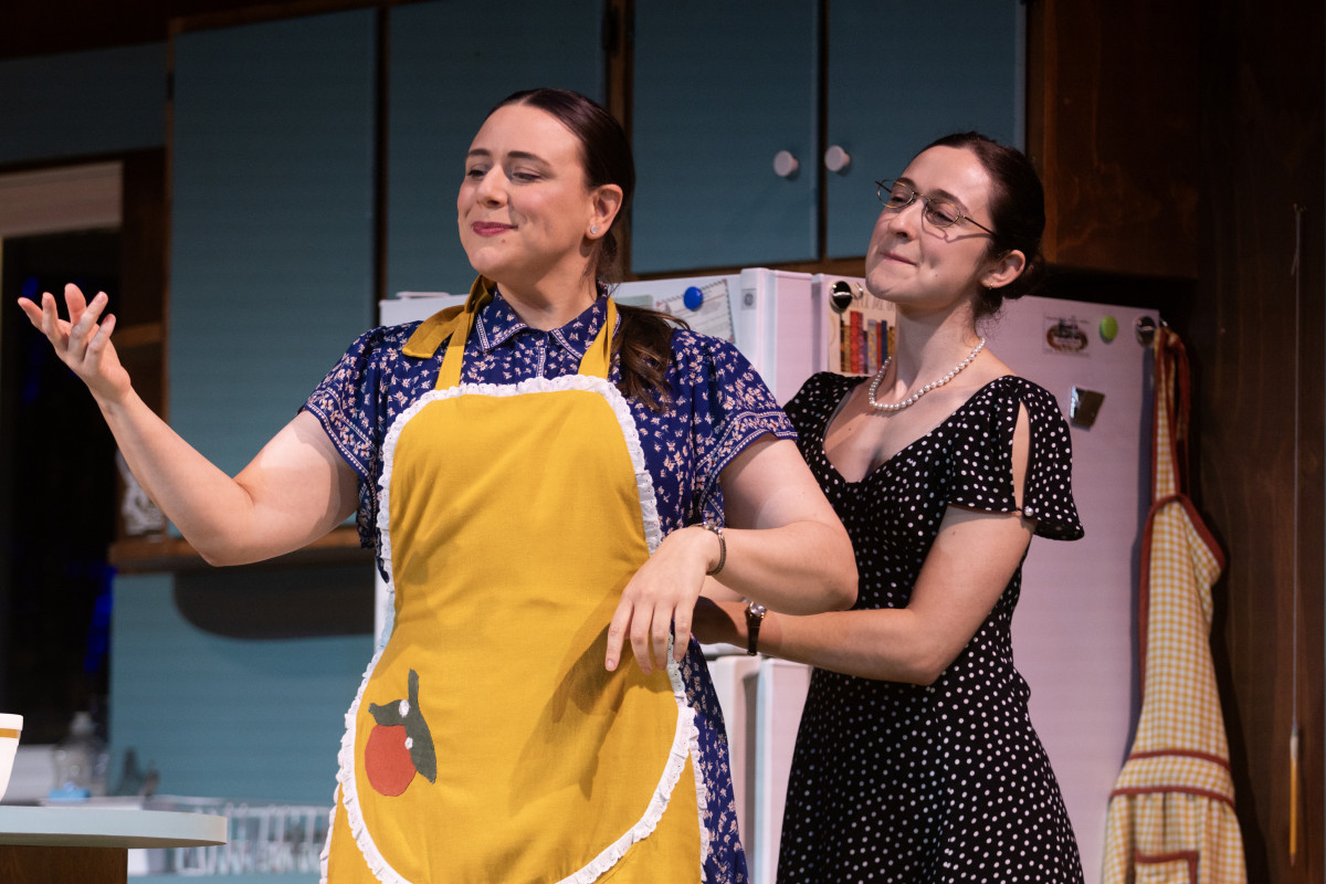 Chautauqua Theater Company Conservatory Actor Amara Leonard — portraying Alice, at right — ties an apron onto Guest Artist Ceci Fernández, portraying Alice’s daughter Ernestine, during the final dress rehearsal for Birthday Candles July 5 in Bratton Theater. 